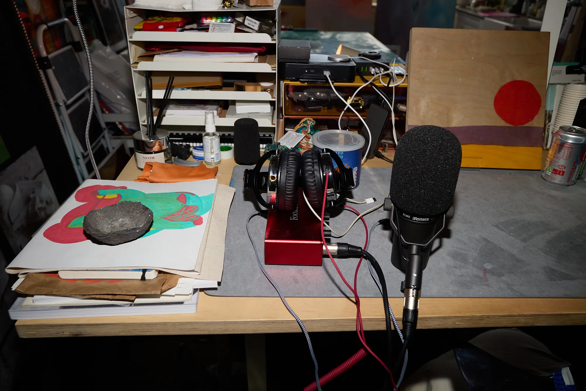 A microphone, headphones and a stone resting on a cluttered studio desk