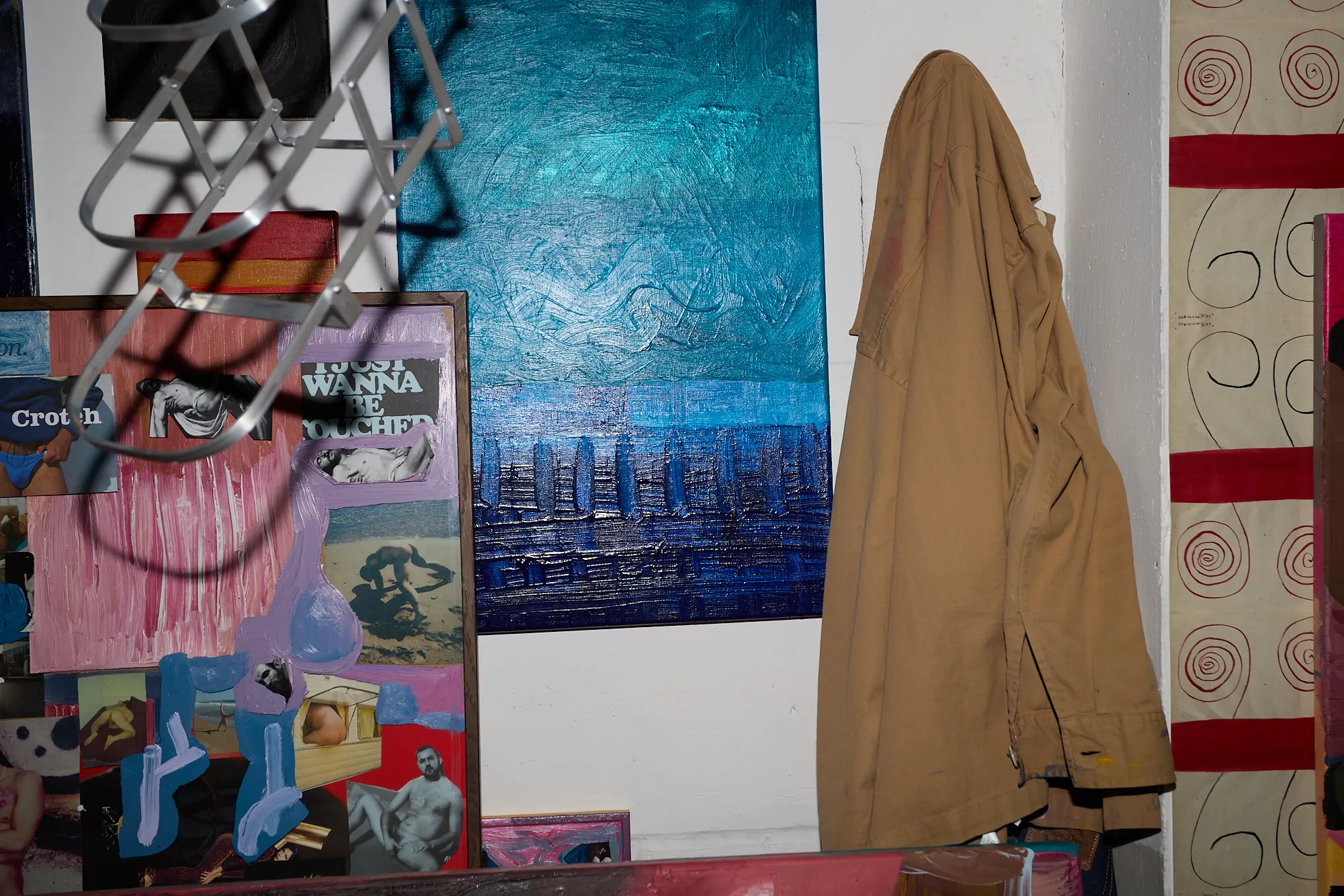 A collage and a large blue painting on the studio wall, beside a jacket hanging from a rack