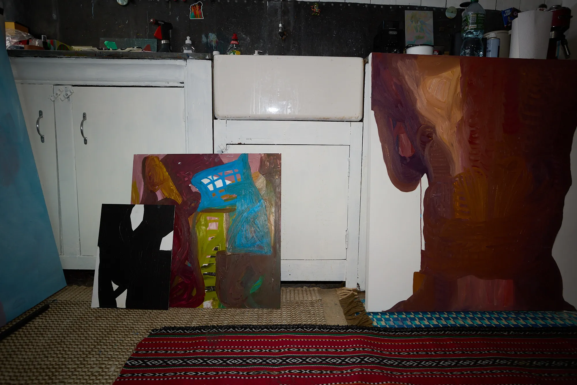 Paintings propped against kitchen cabinets and a sink in Omar Kholeif's studio