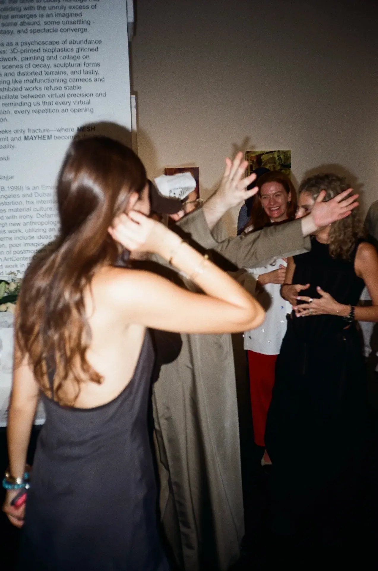 Guests laughing and reaching out to high-five in front of the exhibition wall text
