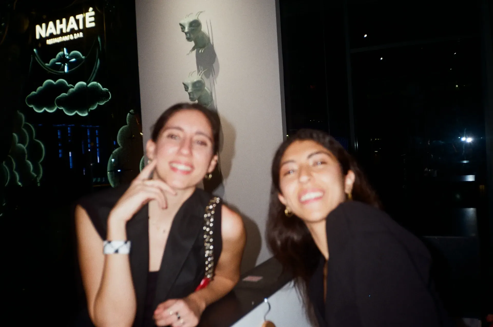 Two guests smiling for a photo at night, with the Nahaté restaurant sign lit up behind them