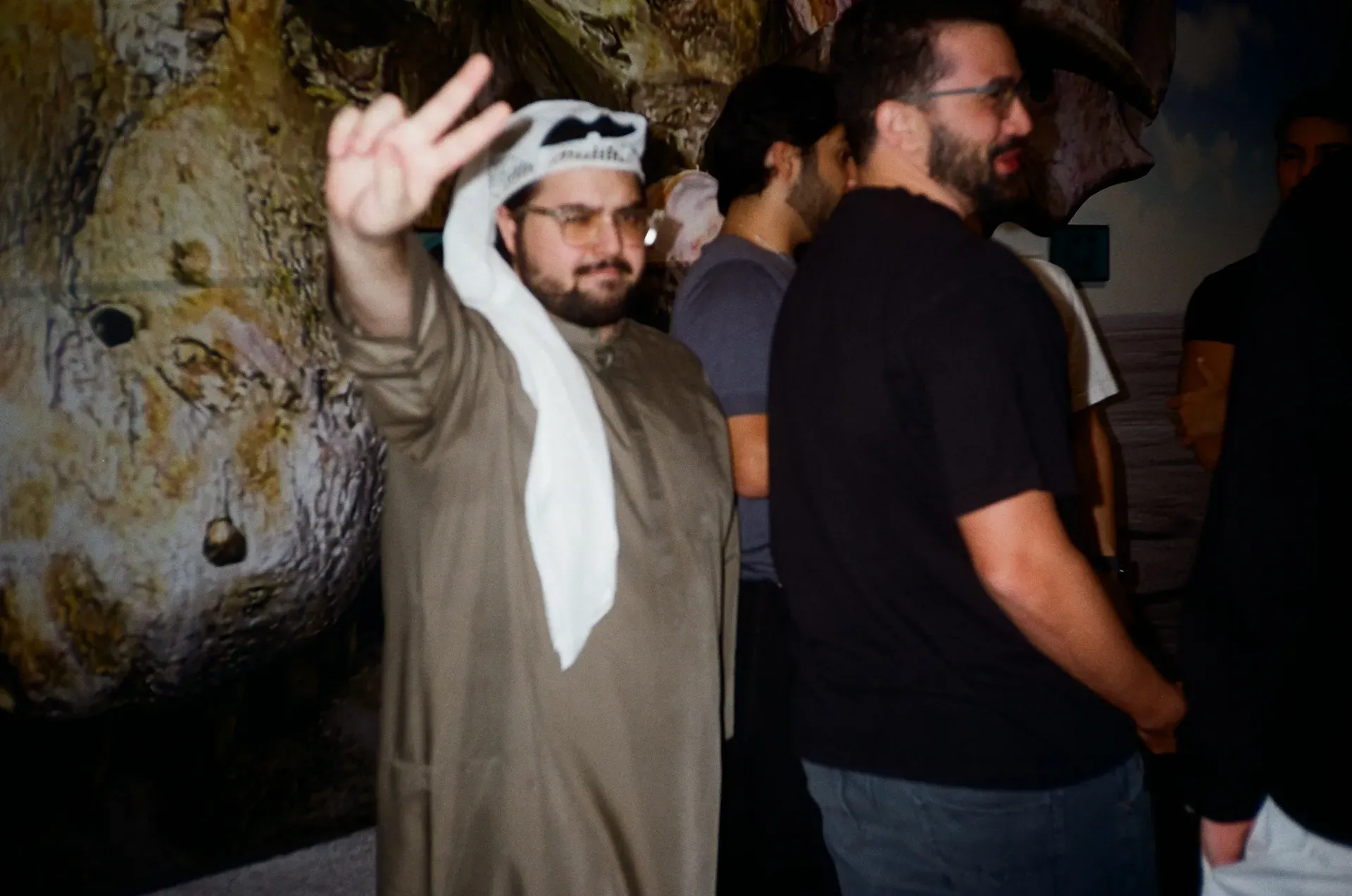 A guest in a keffiyeh giving a peace sign in front of a large sculptural skull