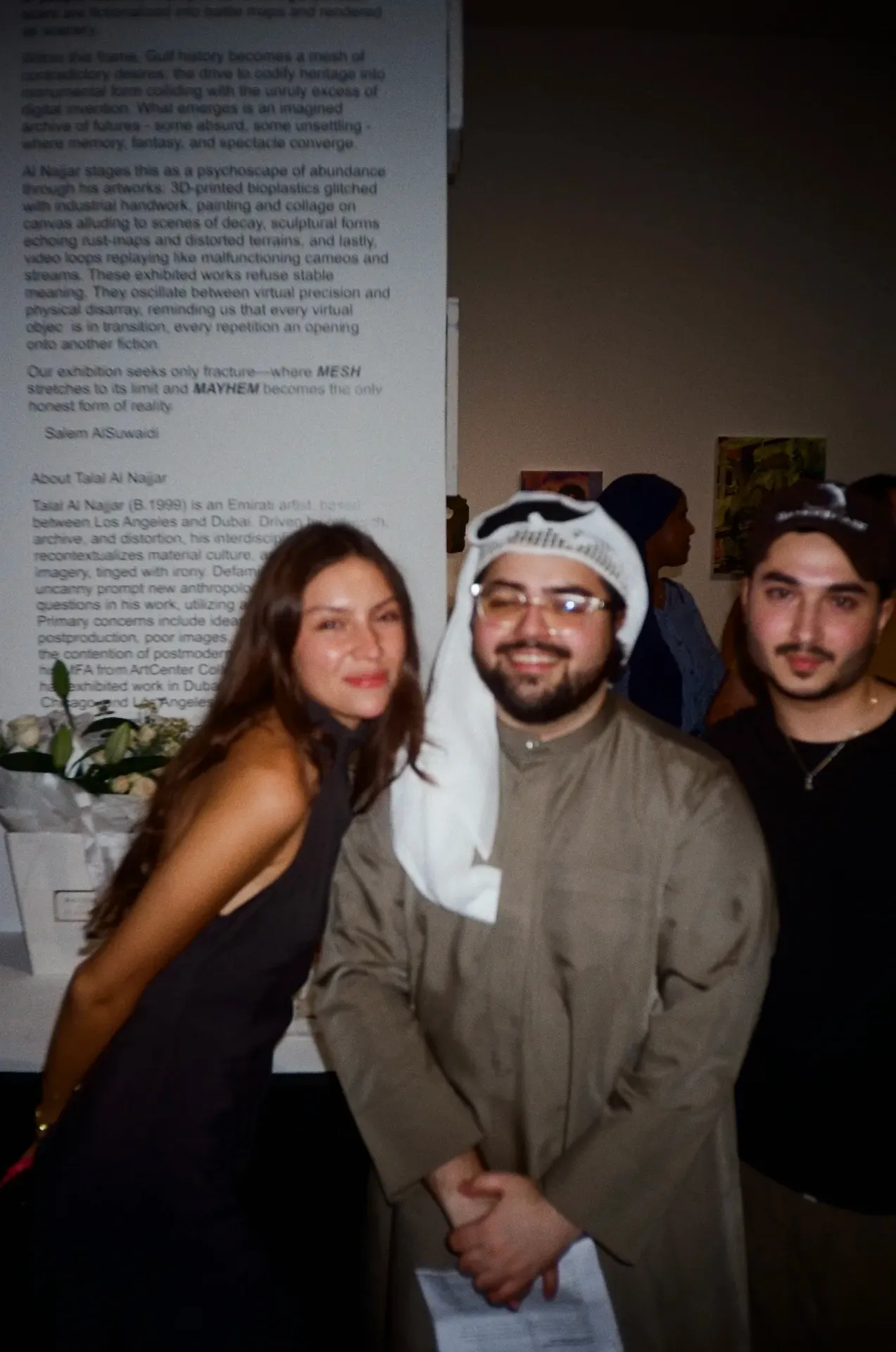 Three guests posing beside the wall text about artist Talal Al Najjar